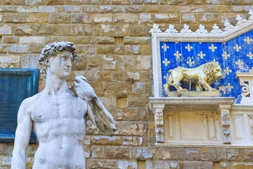 A stone statue of a man holding a bird, next to a lion statue on a stone wall with a blue and white patterned section. 4