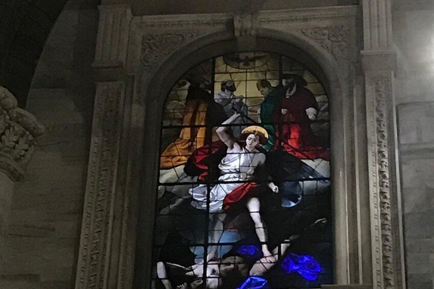 A stained glass window with a central figure, surrounded by other figures and architectural details. 5