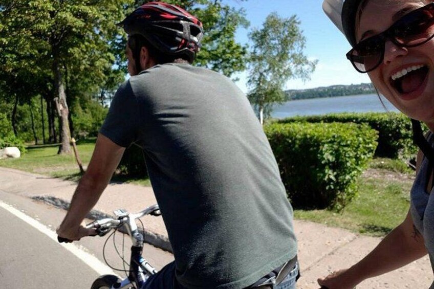 En person cykler på en vej med træer og et vandareal i baggrunden. 2