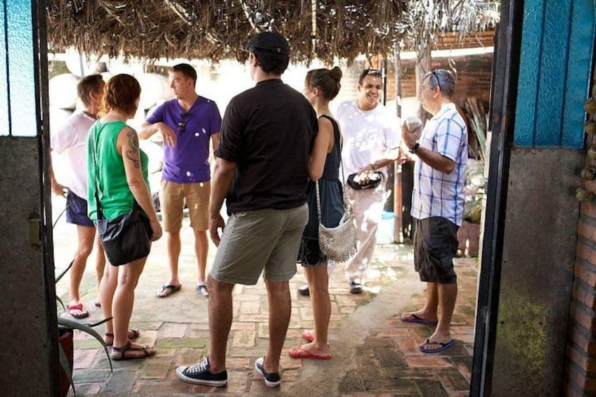 A group of people standing in a covered outdoor area with a brick floor and a thatched roof overhead. 2