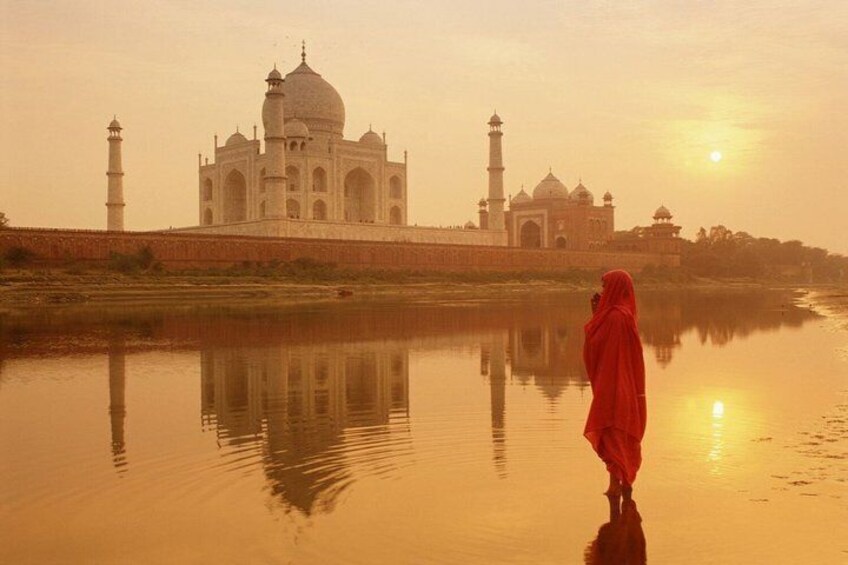 The Taj Mahal with a person in red standing by the water reflecting the structure. 4