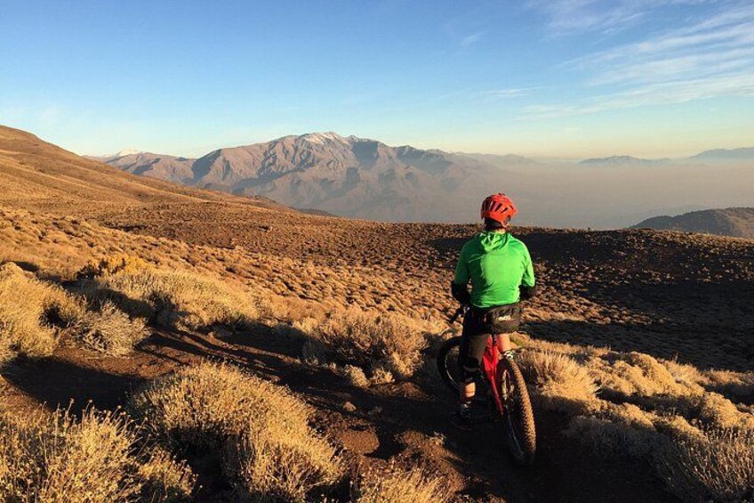 En person cykler på en mountainbike over tørt græsland med fjerne bjerge under en klar himmel. 4