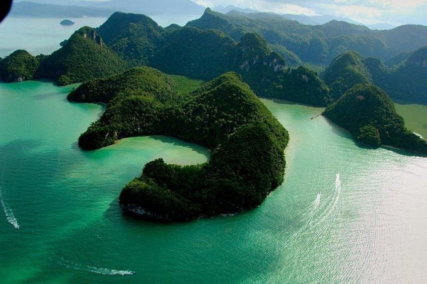 Une vue aérienne d’une île verdoyante entourée d’eaux turquoise, avec un bateau qui laisse une vague derrière lui. 1