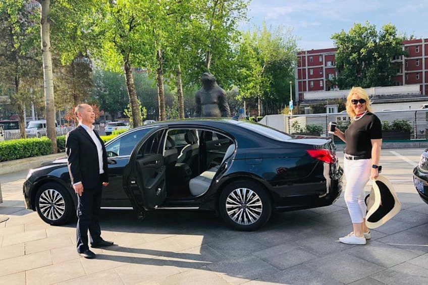 A black car parked on a paved area with trees and a statue in the background. 2