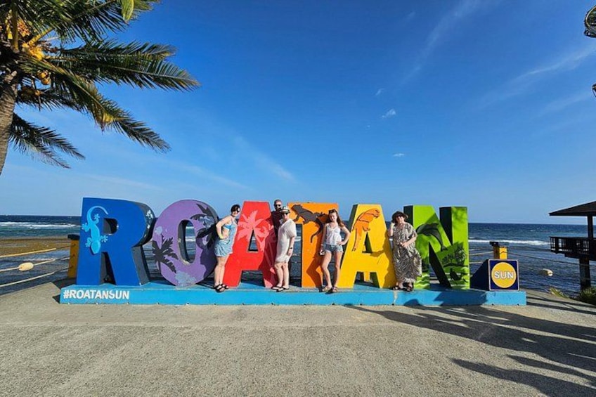 A beach with a colorful sign spelling 'ROCATAN' and palm trees in the background. 2