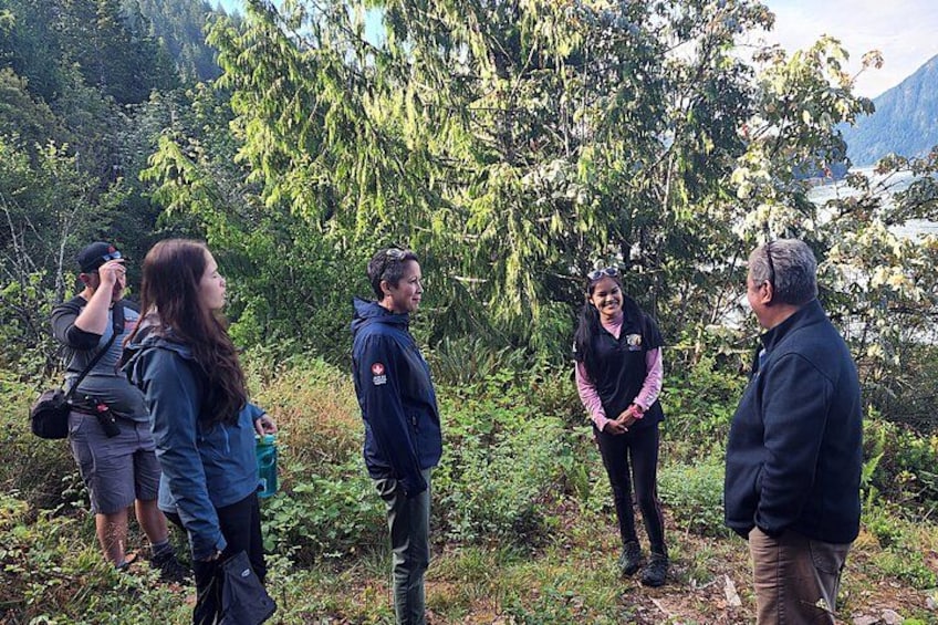Un groupe de personnes se tient à l’extérieur, certaines portent des vestes, et on aperçoit des arbres et des montagnes en arrière-plan. 3