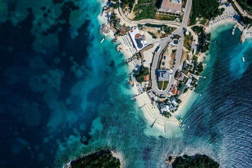 An aerial view of a coastal area with clear blue waters, a sandy beach, and a small town with buildings and roads. 2