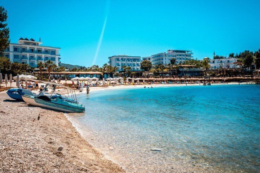 A beach with clear water, a boat, and buildings in the background. 3