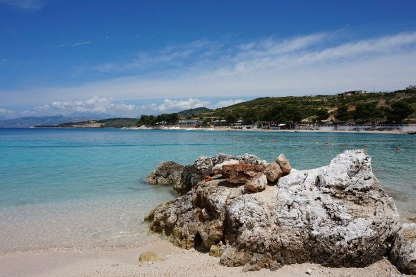 A beach with clear turquoise water, white rocks, and a distant hill with buildings. 4