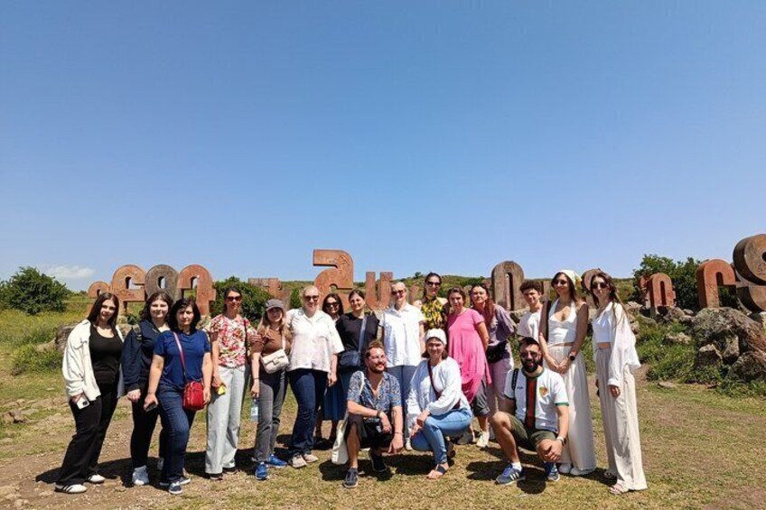 A group of people posing in front of large, rusted metal letters spelling 'FONDA.' 2