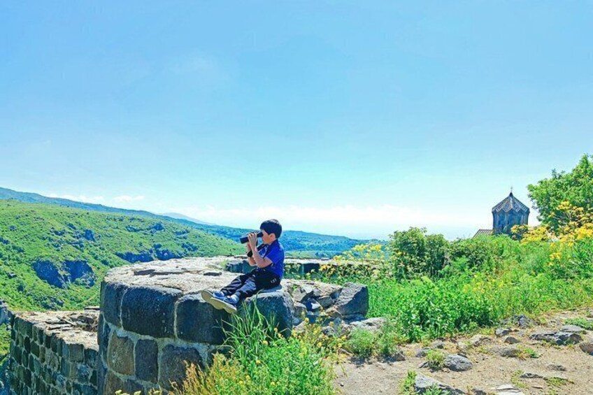 A person sitting on a stone structure overlooking a green landscape with a small building in the distance. 5