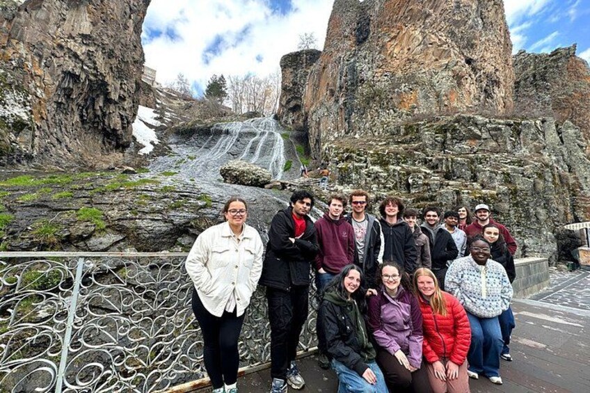 Eine Gruppe von Personen steht vor einer felsigen Landschaft mit einem Wasserfall. 3