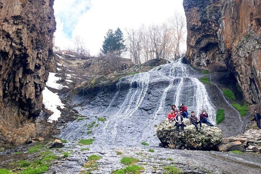 Ein Wasserfall stürzt über eine felsige Hangseite, während Menschen auf einer Felsformation sitzen. 2