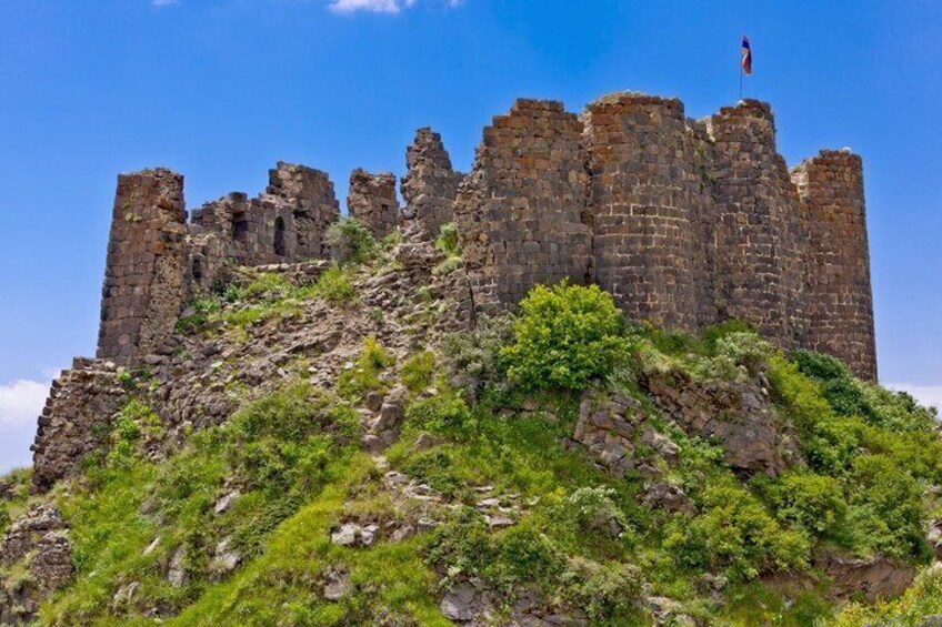 A historic stone castle atop a grassy hill with a clear sky. 4