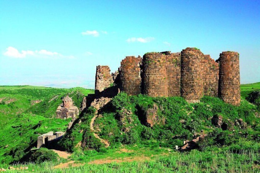 A medieval castle with ruins, surrounded by lush green hills and a clear sky. 1