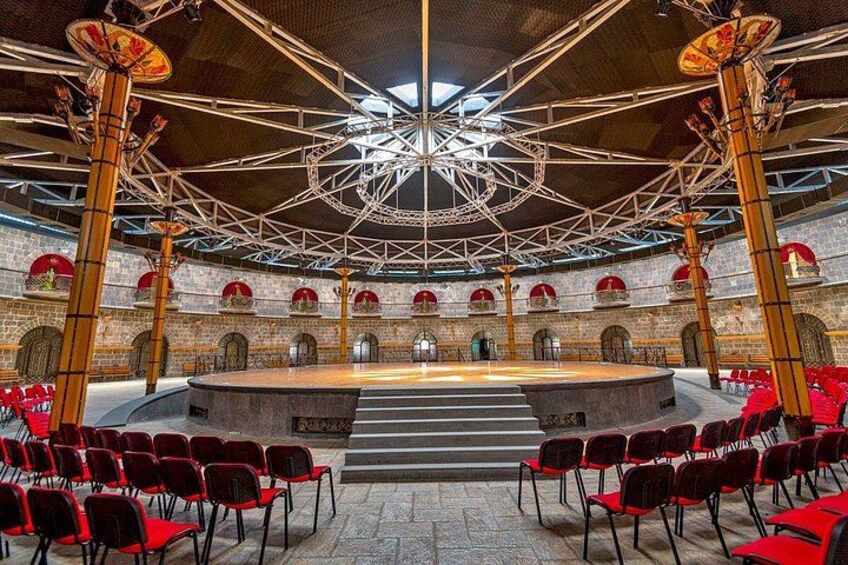 A large hall with a central stage, red chairs, and a complex ceiling structure. 2