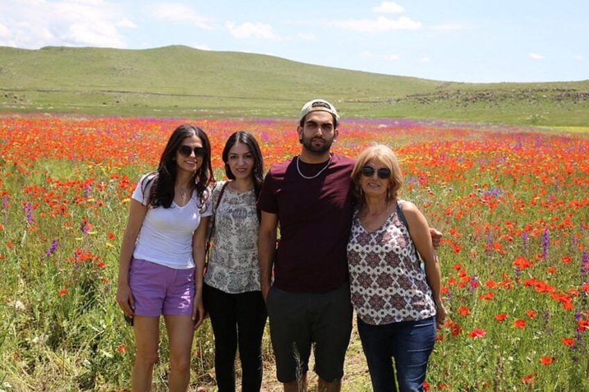 A group of people standing in a field of red flowers with green hills in the background. 4