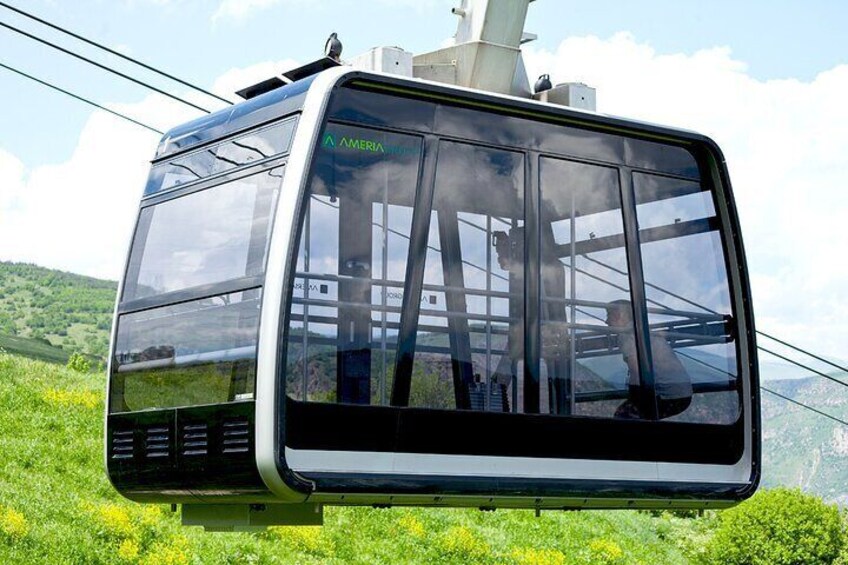 A cable car with "AMERIMANIA" written on the side, suspended by cables against a backdrop of green hills and a clear sky. 2