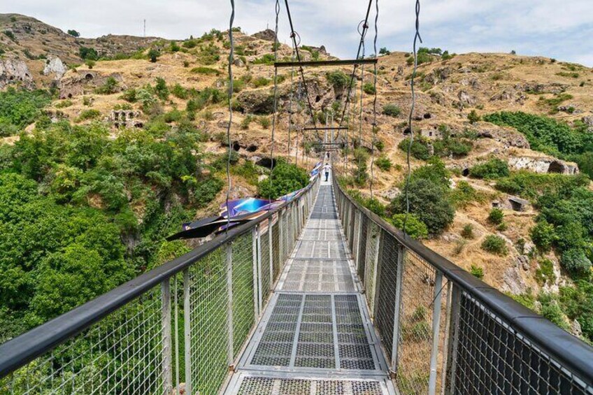 A suspension bridge with metal railings and a metal walkway, surrounded by green vegetation and rocky terrain. 5