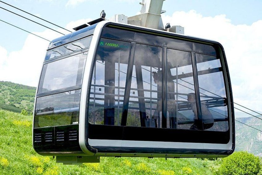 A cable car with 'AMERIA' written on it, suspended by cables, with a mountainous landscape in the background. 2
