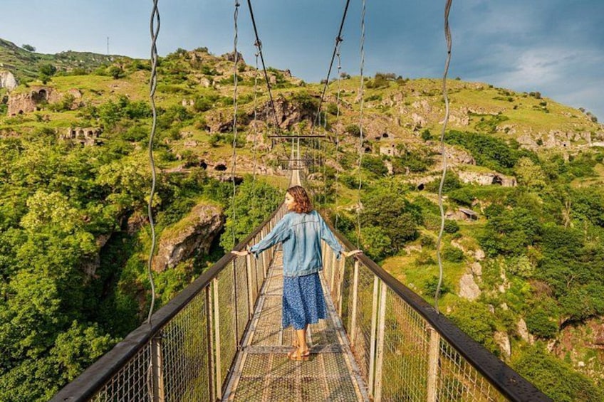 A person walking on a suspension bridge with a mountainous landscape in the background. 1
