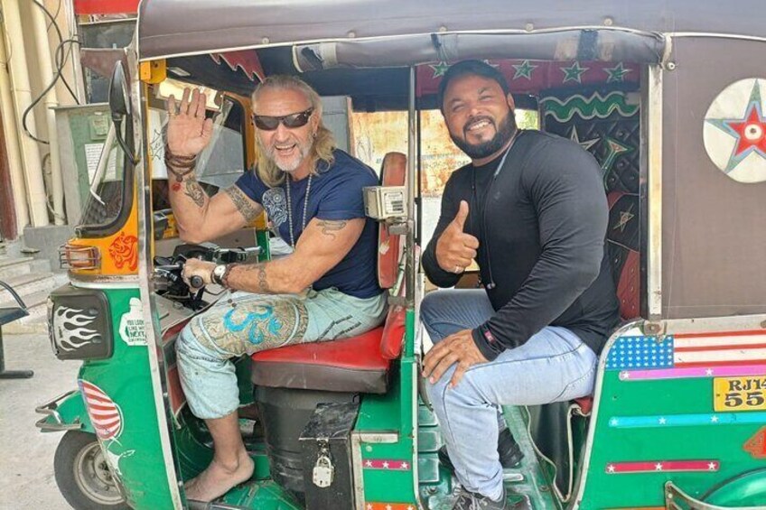 To mænd i en grøn og rød auto-rickshaw, hvoraf den ene giver et tommelfingerop. 1