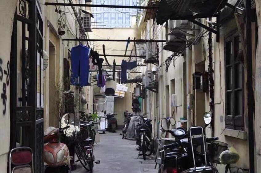 A narrow alley with bicycles parked on both sides, a motorcycle, and hanging laundry. 1