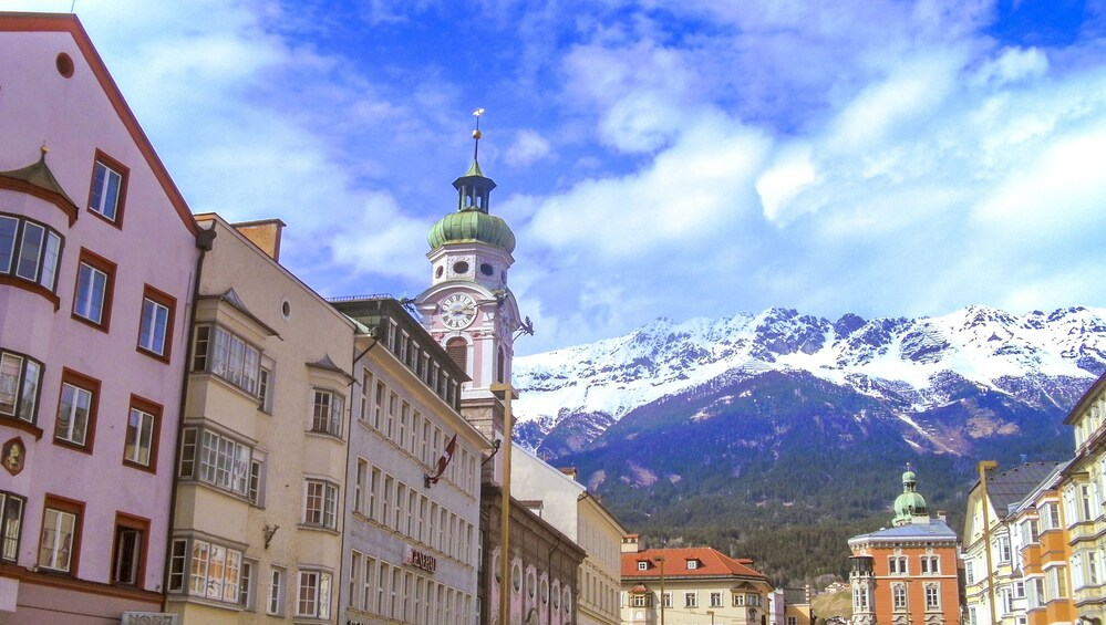 Una calle con edificios históricos y una torre del reloj, con montañas nevadas al fondo. 4