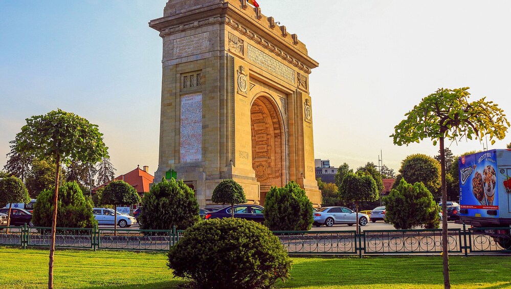 A large monument with inscriptions, surrounded by trees and cars. 2