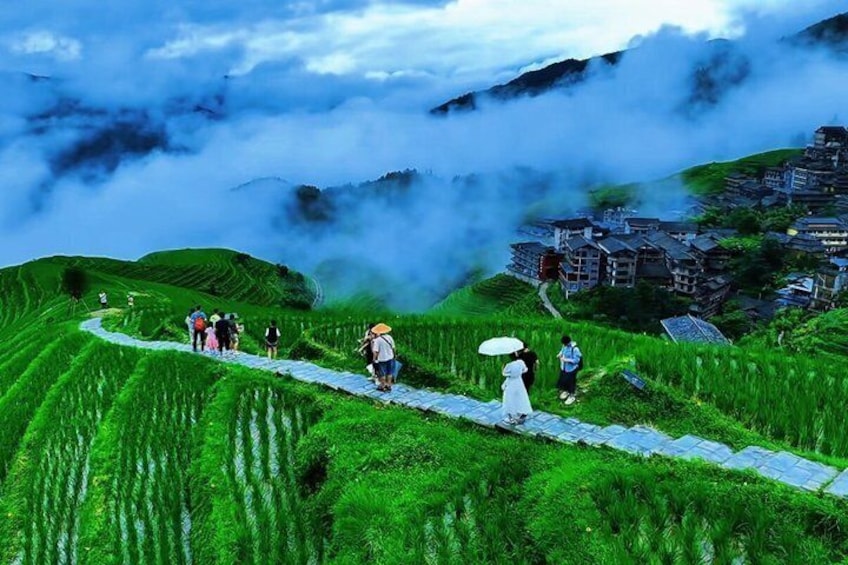 A group of people walking on a path through lush green rice terraces with mist-covered mountains in the background. 3