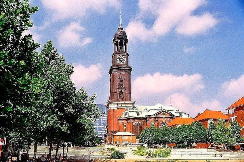 A historic clock tower, a church, and surrounding trees. 4