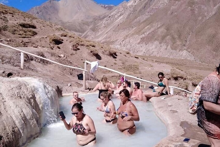 Un grupo de personas sentadas en una fuente termal rodeada de montañas. 2