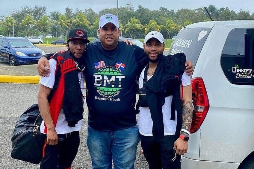 Three people standing in front of a white vehicle with a logo on the back. 2