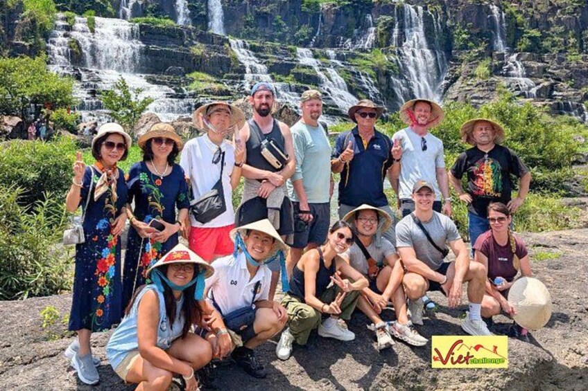 Un grupo de personas posando frente a una cascada, con abundante vegetación de fondo. 2