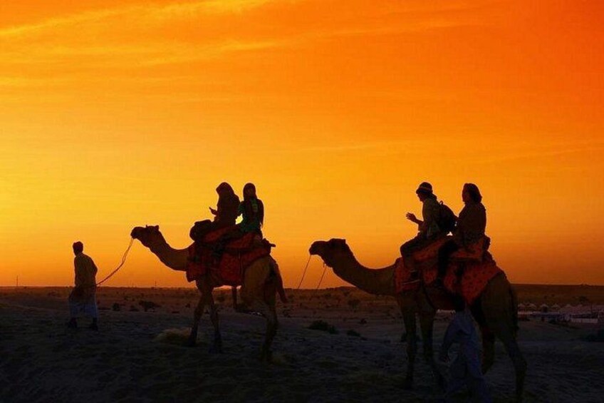 A camel caravan at sunset with riders and a guide. 2
