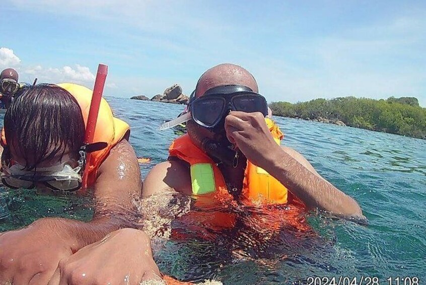 Två personer som snorklar i klart vatten, med klippor och grönska i bakgrunden. 4