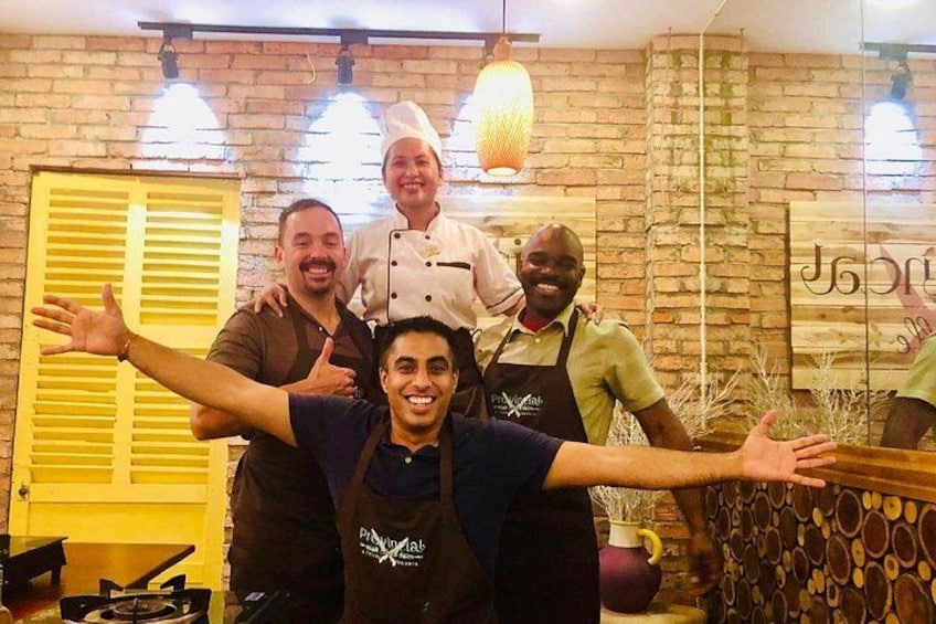 Un groupe de personnes se trouve dans une cuisine aux murs en briques, avec un luminaire suspendu et une porte jaune. 3