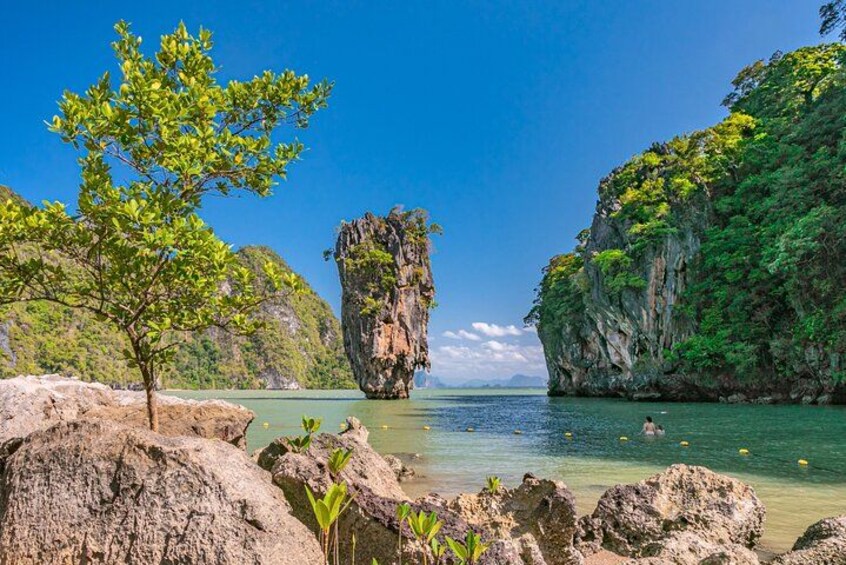 A coastal landscape with a prominent rock formation, clear water, and lush greenery. 1