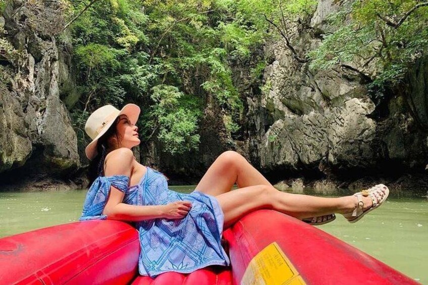 A person in a blue dress and hat sitting on a red inflatable raft in a river surrounded by rocky cliffs and greenery. 4