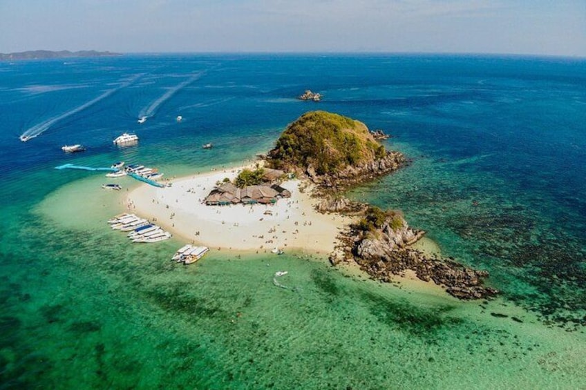 Luchtbeeld van een tropisch eiland met helder turquoise water, een zandstrand en verschillende boten die vlakbij de kust afgemeerd liggen. 1