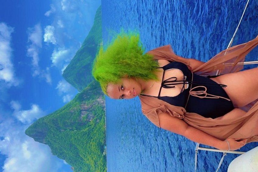 A person with green hair on a boat with a blue ocean and green land in the background. 2