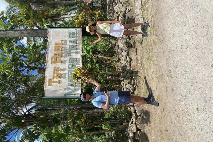 A sign with the text 'Ter Pau Nature Trail' and two people standing in front of it. 5