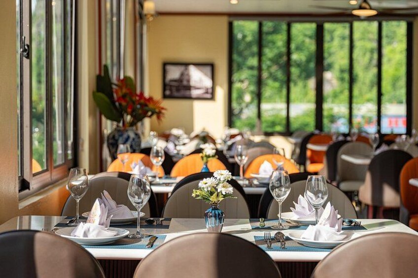 A restaurant with tables set for dining, chairs, and a view of greenery outside. 5