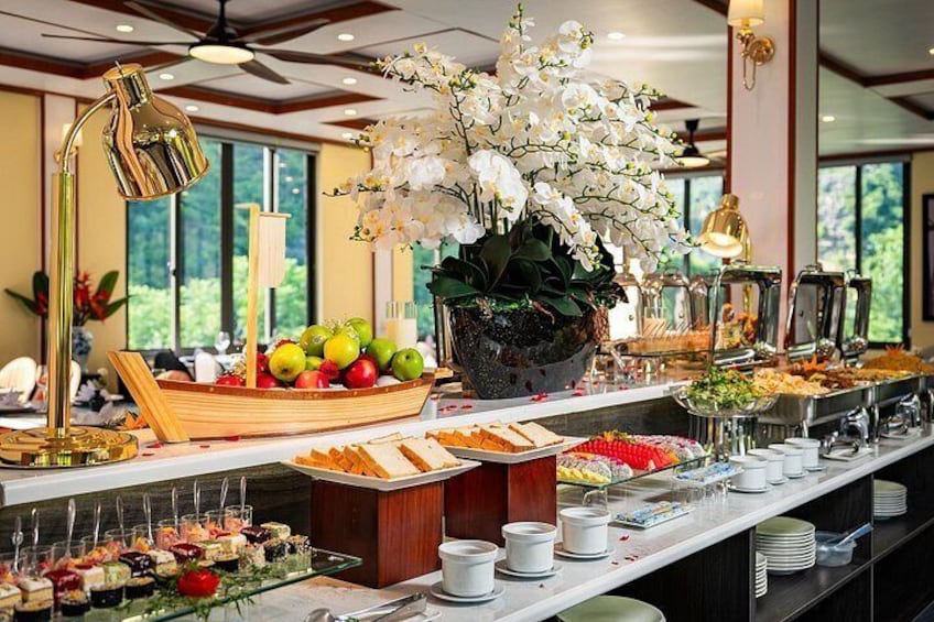 A buffet with various food items, a large orchid plant, and a window with a view of greenery. 3