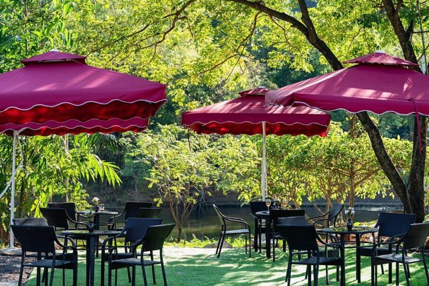 Outdoor dining tables with chairs and red umbrellas, surrounded by trees. 5