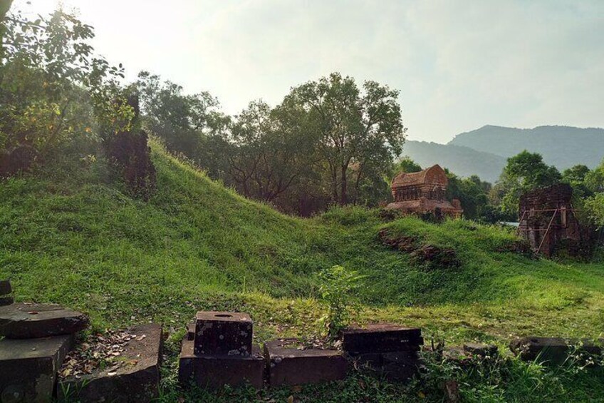 A grassy hill with ancient ruins and a small structure in the distance. 5
