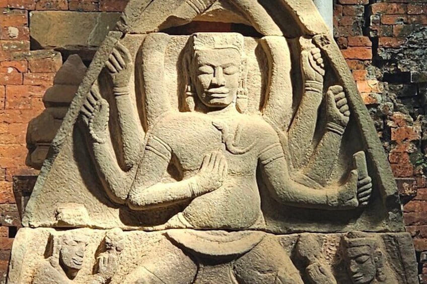 A stone sculpture of a figure with multiple arms, set against a brick wall. 1