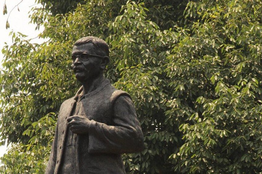 Una statua di un uomo in abito che si trova di fronte a un albero. 3