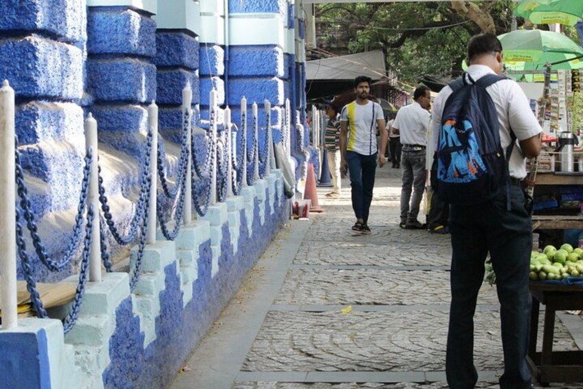 Une rue pavée bordée d’un mur bleu et blanc, un homme avec un sac à dos et un étal de fruits. 4