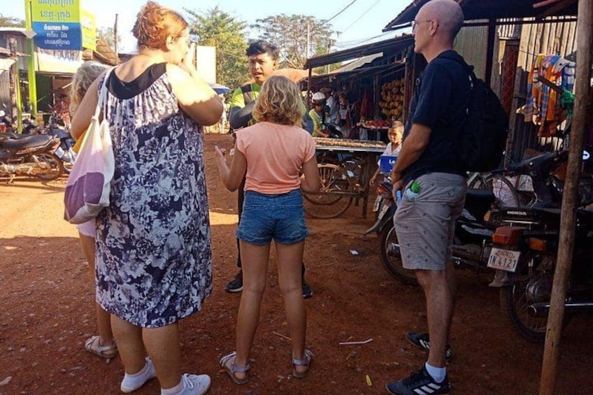 A group of people standing in a market area with a dirt ground, a motorcycle, and a bicycle. 3